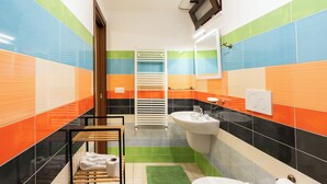 Een badkamer met kleurrijke tegels, een wastafel, toilet, handdoekhouder en een spiegel.