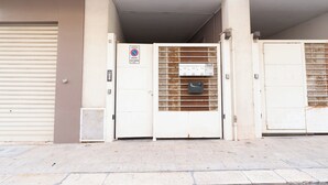 Een gevel met een gesloten garagepoort, een metalen hek met een bord en een ventilatiesysteem.