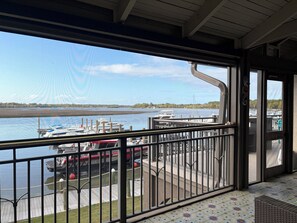 Ein überdachter Außenbereich mit Blick auf Boote, die in einer Marina vor Anker liegen, ein Holzdeck und ein Geländer.