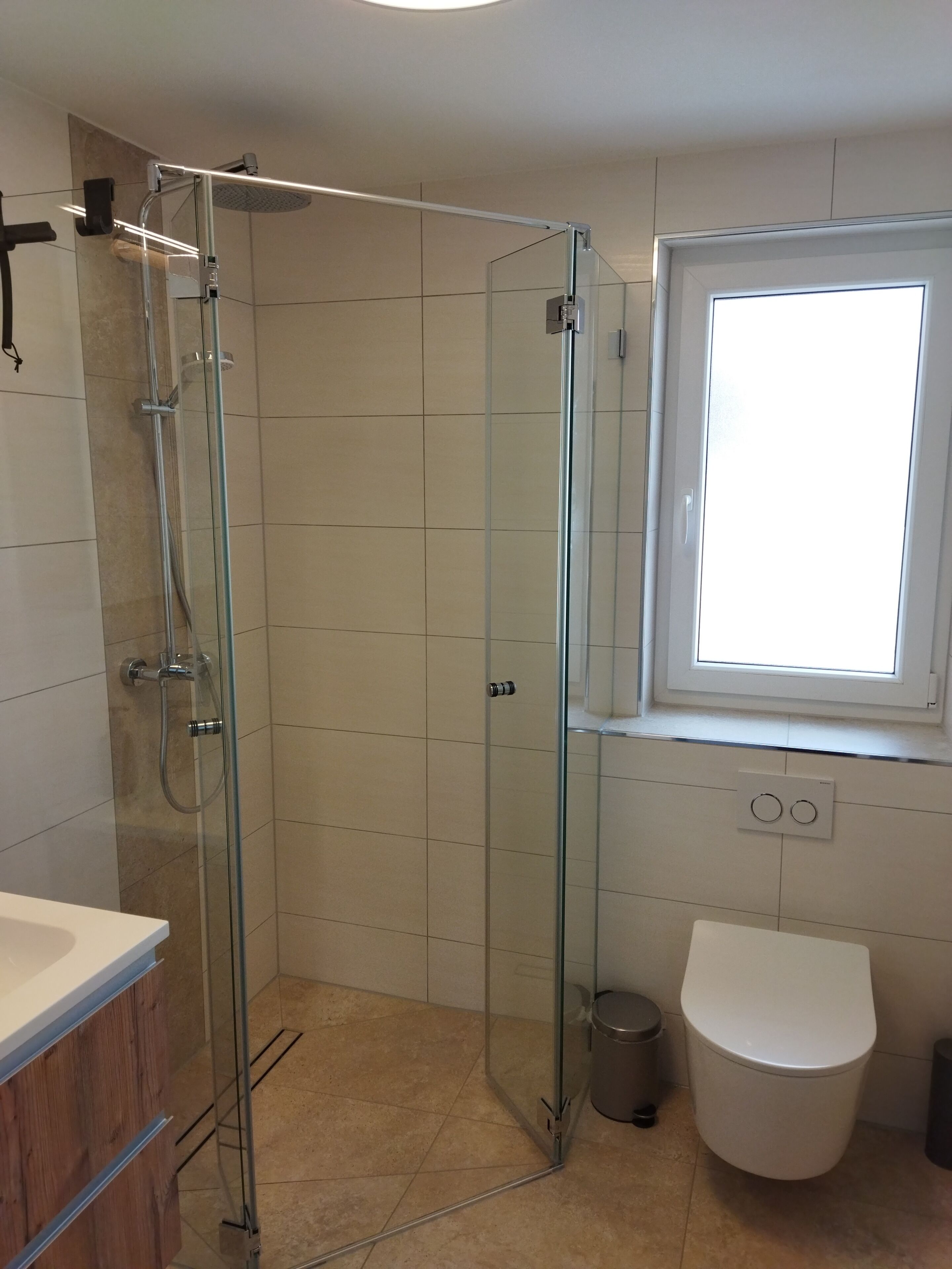 Un bagno moderno con doccia vetrata, un water bianco e una finestra che lascia entrare luce naturale.
