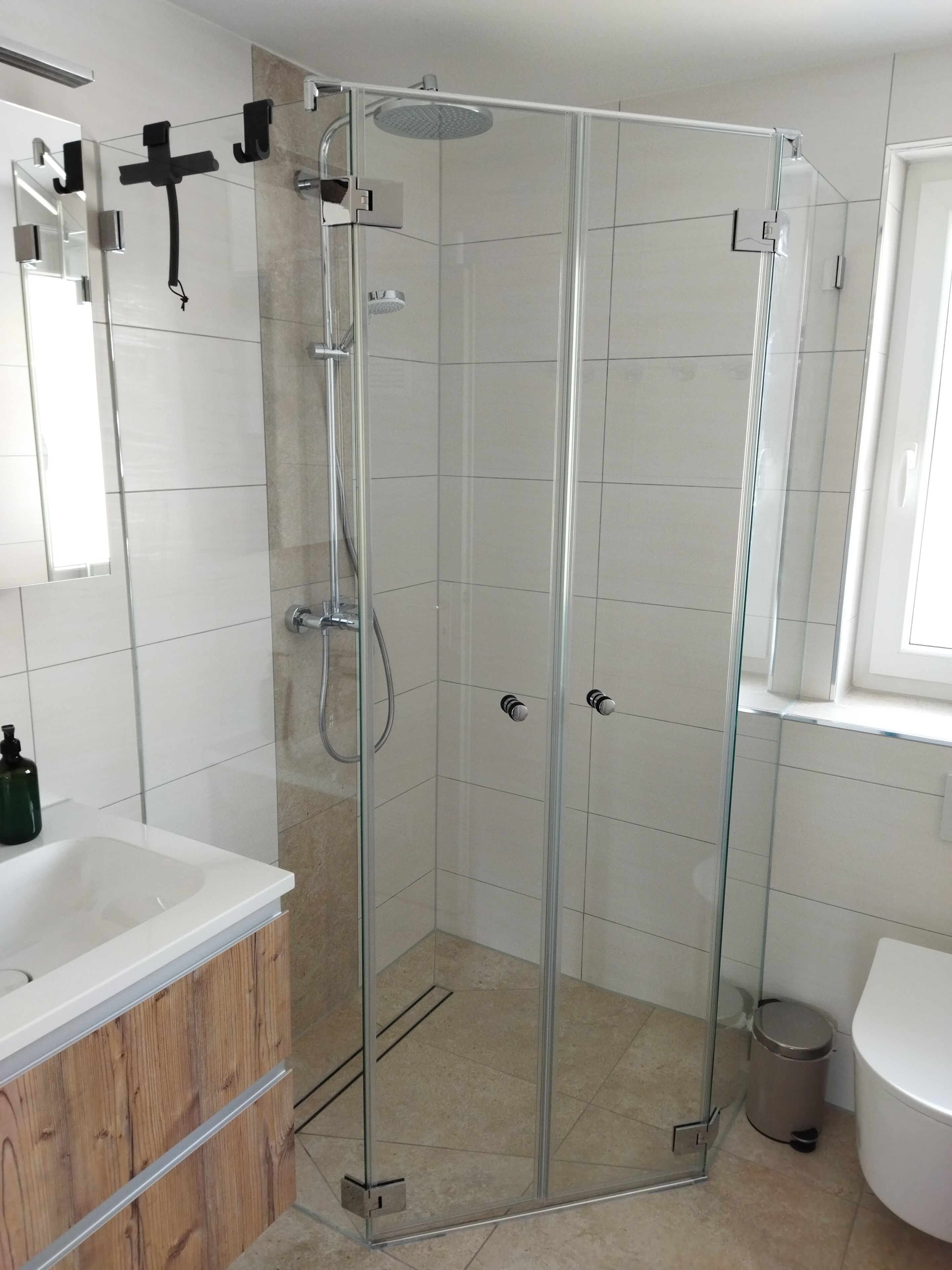 Une cabine de douche fermée par des parois en verre, dotée d’un pommeau de douche à main, d’un porte-serviettes fixé au mur et d’un WC visible dans la pièce adjacente.