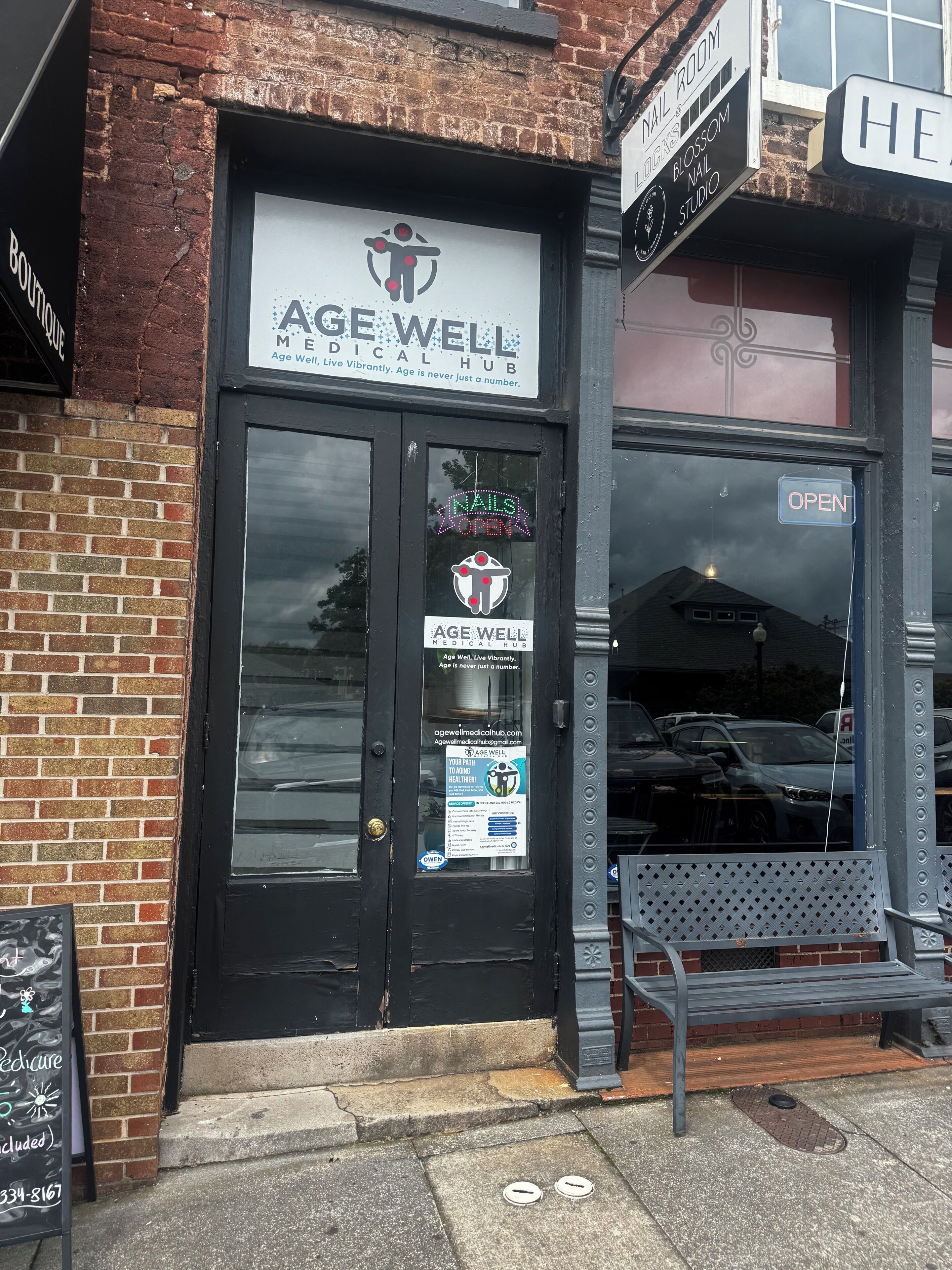 Un escaparate con un cartel que dice 'AGE WELL MEDICAL HUB' y un cartel que indica 'NAILS OPEN'.