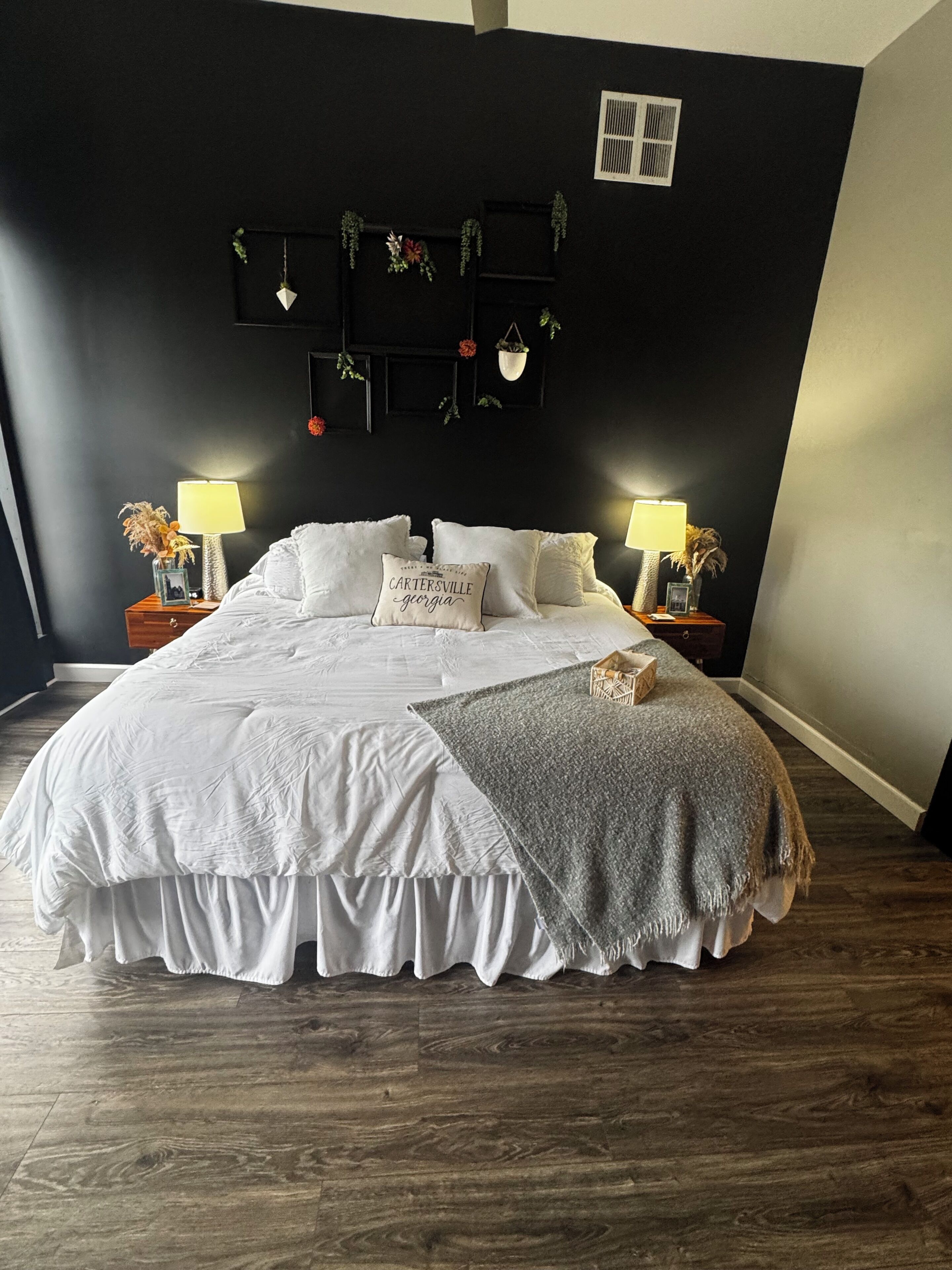 Ein Schlafzimmer mit einem großen Bett, zwei Nachttischen mit Lampen, einer dunklen Wand mit einem dekorativen Regal und einem Holzboden.