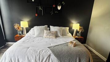 Ein Schlafzimmer mit einem großen Bett, zwei Nachttischen mit Lampen, einer dunklen Wand mit einem dekorativen Regal und einem Holzboden.