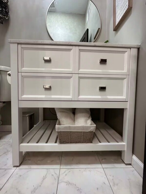 A white vanity with four drawers, a mirror, and a wicker basket underneath. - Historic Downtown Loft in Cartersville (Cartersville)