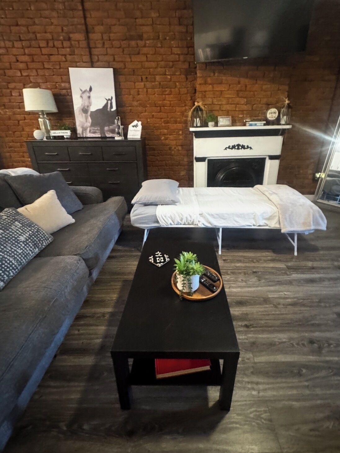 A living room with a brick wall, a sofa, a coffee table with a plant, and a fireplace.
