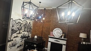 A dining area with a wooden table, chairs, a wall mural, a fireplace, and two hanging light fixtures. - Historic Downtown Loft in Cartersville (Cartersville)