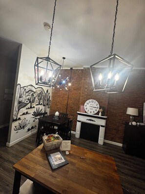 A dining area with a wooden table, chairs, a wall mural, a fireplace, and two hanging light fixtures. - Historic Downtown Loft in Cartersville (Cartersville)