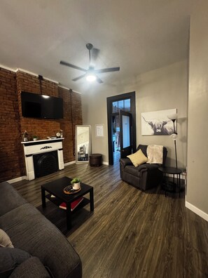 A living room with a fireplace, a flat-screen TV, a ceiling fan, and a sofa. - Historic Downtown Loft in Cartersville (Cartersville)