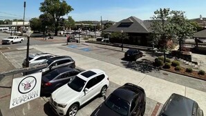 A parking lot with several cars, a building with a dark roof, and a sign for 'Heaven Scents Cupcakes.' - Historic Downtown Loft in Cartersville (Cartersville)