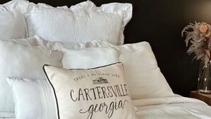 A bed with white bedding and a pillow with 'CARTERSVILLE georgia' text. - Historic Downtown Loft in Cartersville (Cartersville)