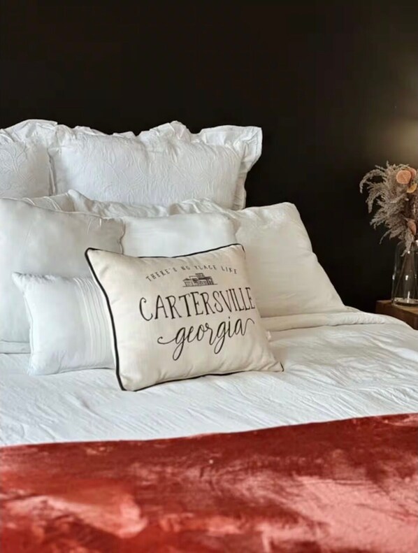 A bed with white bedding and a pillow with 'CARTERSVILLE georgia' text. - Historic Downtown Loft in Cartersville (Cartersville)