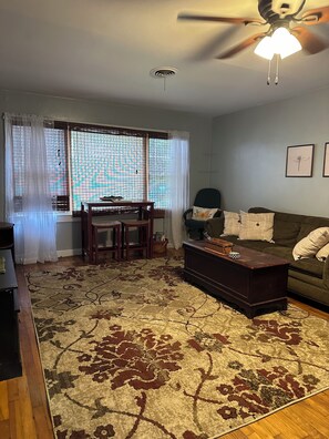 A living room with a ceiling fan, a dining table with chairs, a sofa, and a patterned rug.