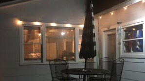 Un patio al aire libre con mesa, sillas, una sombrilla metálica y luces colgantes.