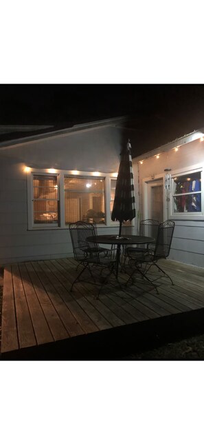 An outdoor patio with a table and chairs, a metal umbrella, and string lights.