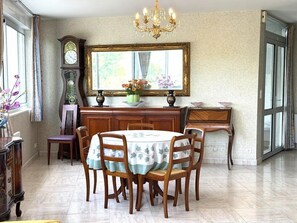 Een eetgedeelte met een ronde tafel, stoelen, een kroonluchter, een klok en een spiegel.