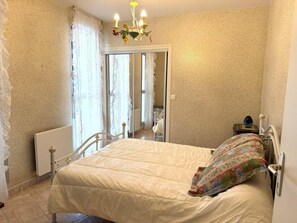 A bedroom with a bed, a radiator, a chandelier, and a door leading to another room. - Apartment for 6 people, 50 m from the coastal path and 500 m from Fort-Bloqué beach, Wi-Fi,... (PLOEMEUR)
