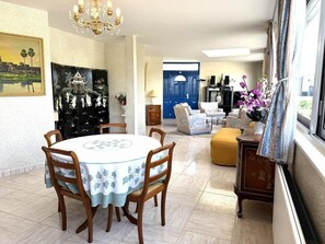 Een eetruimte met een ronde tafel, stoelen, een kroonluchter en een schilderij aan de muur.