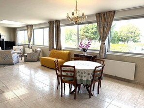Een woonkamer met een bank, stoelen, een eettafel en een kroonluchter.