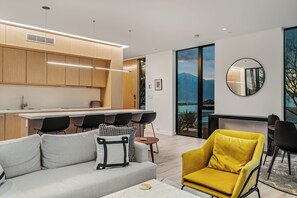 A modern kitchen with wooden cabinets, a dining area with black chairs, a sofa with patterned cushions, and a yellow armchair. - Forbes Featured 3D Home Pool, Spa, Casita Retreat (Desert Hot Springs)