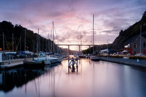 Ein Hafen mit vertäuten Booten, eine Brücke im Hintergrund und ein Gebäude mit einem Schild.