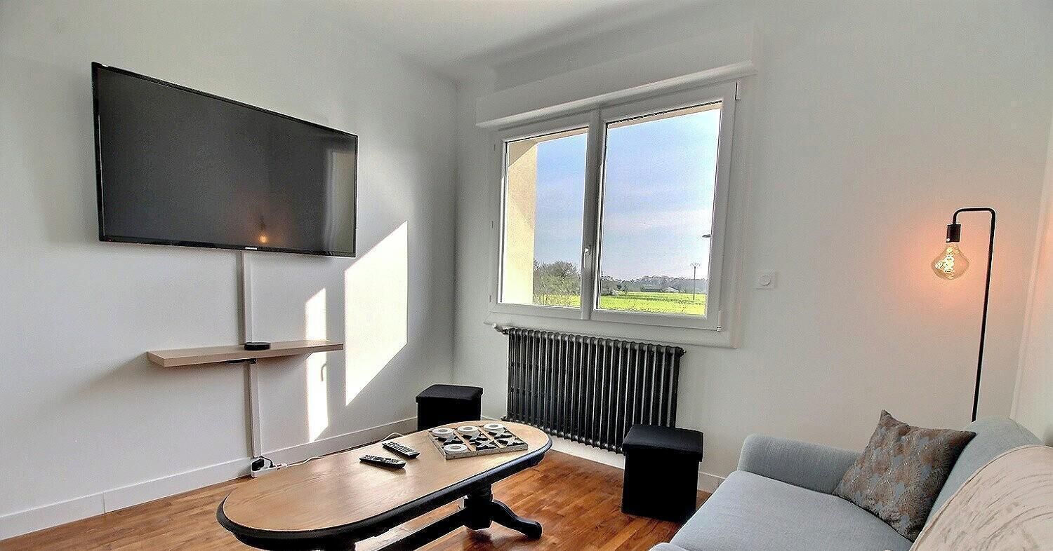 A modern living room with a flat-screen TV, a wooden table with remote controls, a sofa, and a radiator.