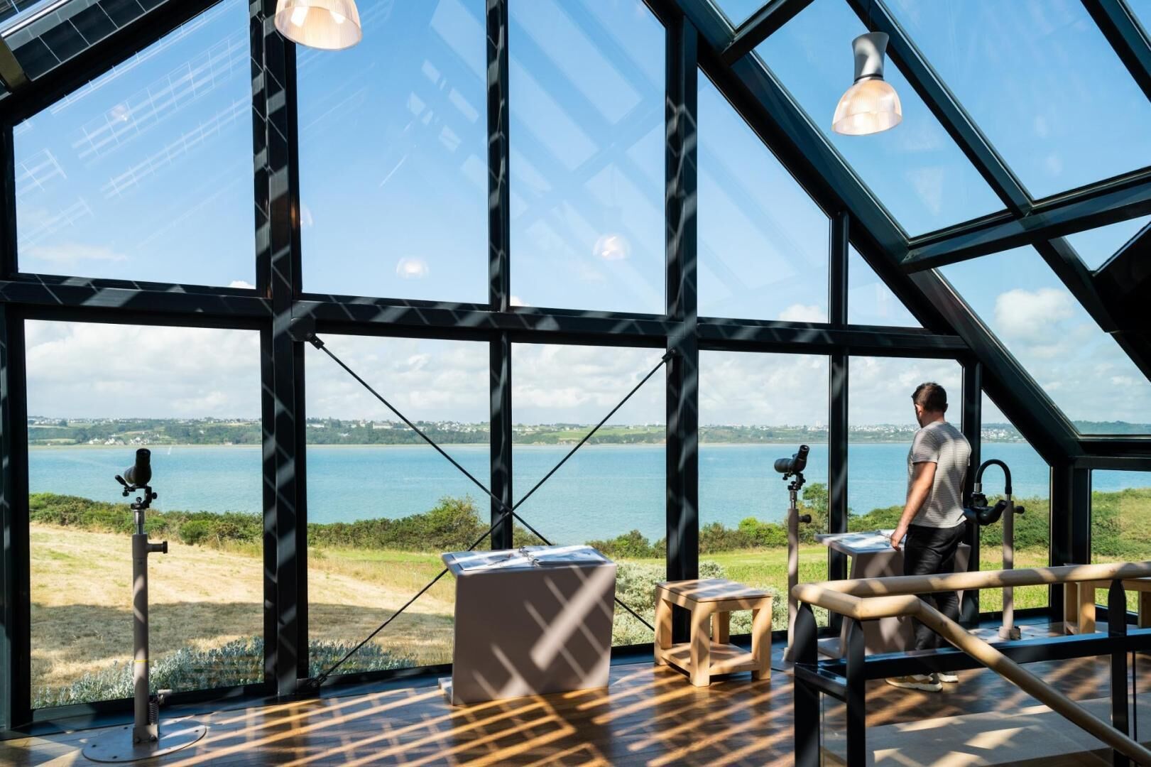 A modern interior with large windows offering a view of a lake and distant landscape.
