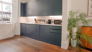 Une cuisine moderne avec des meubles de couleur sombre, un plan de travail équipé d’appareils électrom énagers et une grande fenêtre.
