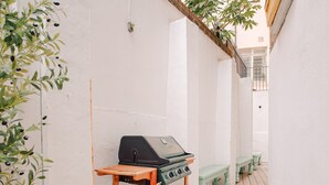 Une étroite terrasse en bois, agrémentée d’un chariot-barbecue, de bancs verts et de plantes en pot.