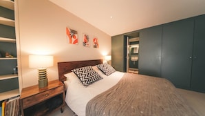 Une chambre à coucher comprenant un lit, des tables de chevet, une lampe, une armoire et des œuvres d’art murales.