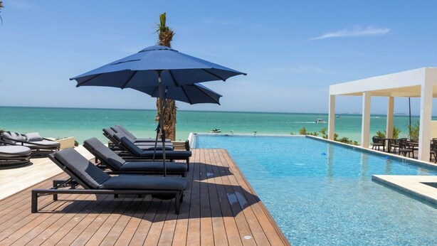 A poolside area with lounge chairs and an umbrella, overlooking a clear blue ocean.