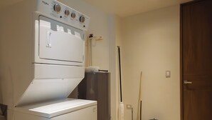 A laundry area with a front-loading washer and dryer, a broom, a mop, and a trash can.