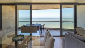 A modern interior with a glass wall, a dining area, and a view of the sea.
