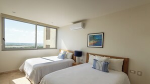 A hotel room with two beds, a large window, an air conditioner, and a painting on the wall.