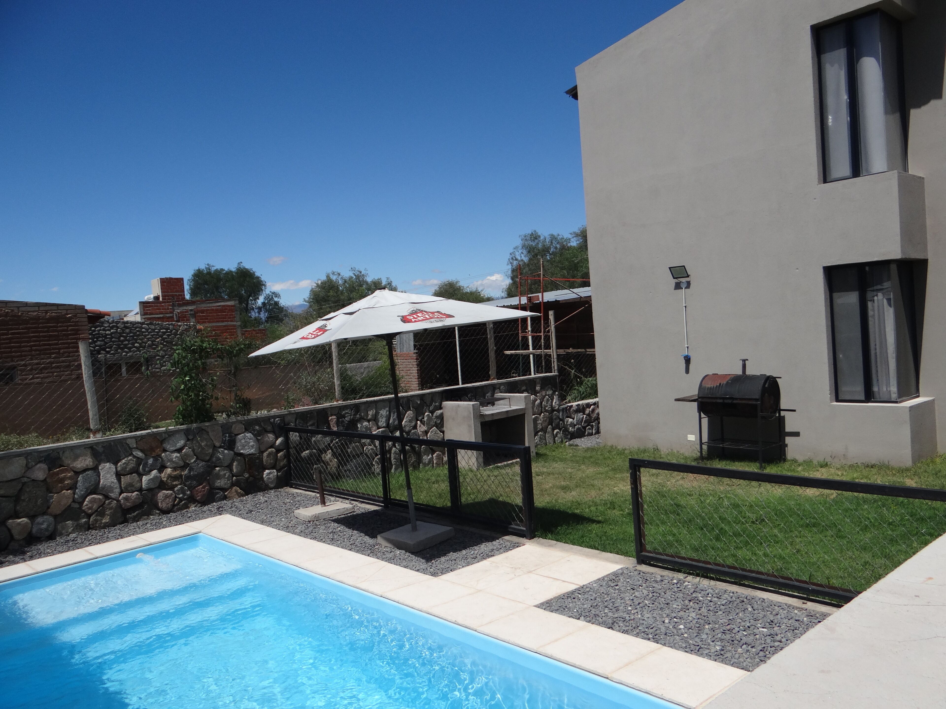 A swimming pool with a stone border, a barbecue grill, and a modern building with a window.