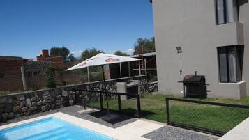A swimming pool with a stone border, a barbecue grill, and a modern building with a window.