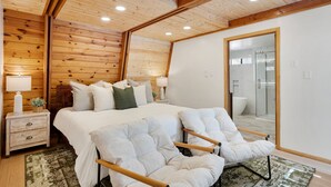 Een slaapkamer met een houten plafond, een groot bed met wit beddengoed, twee nachtkastjes met lampen, en een spiegel aan de muur.