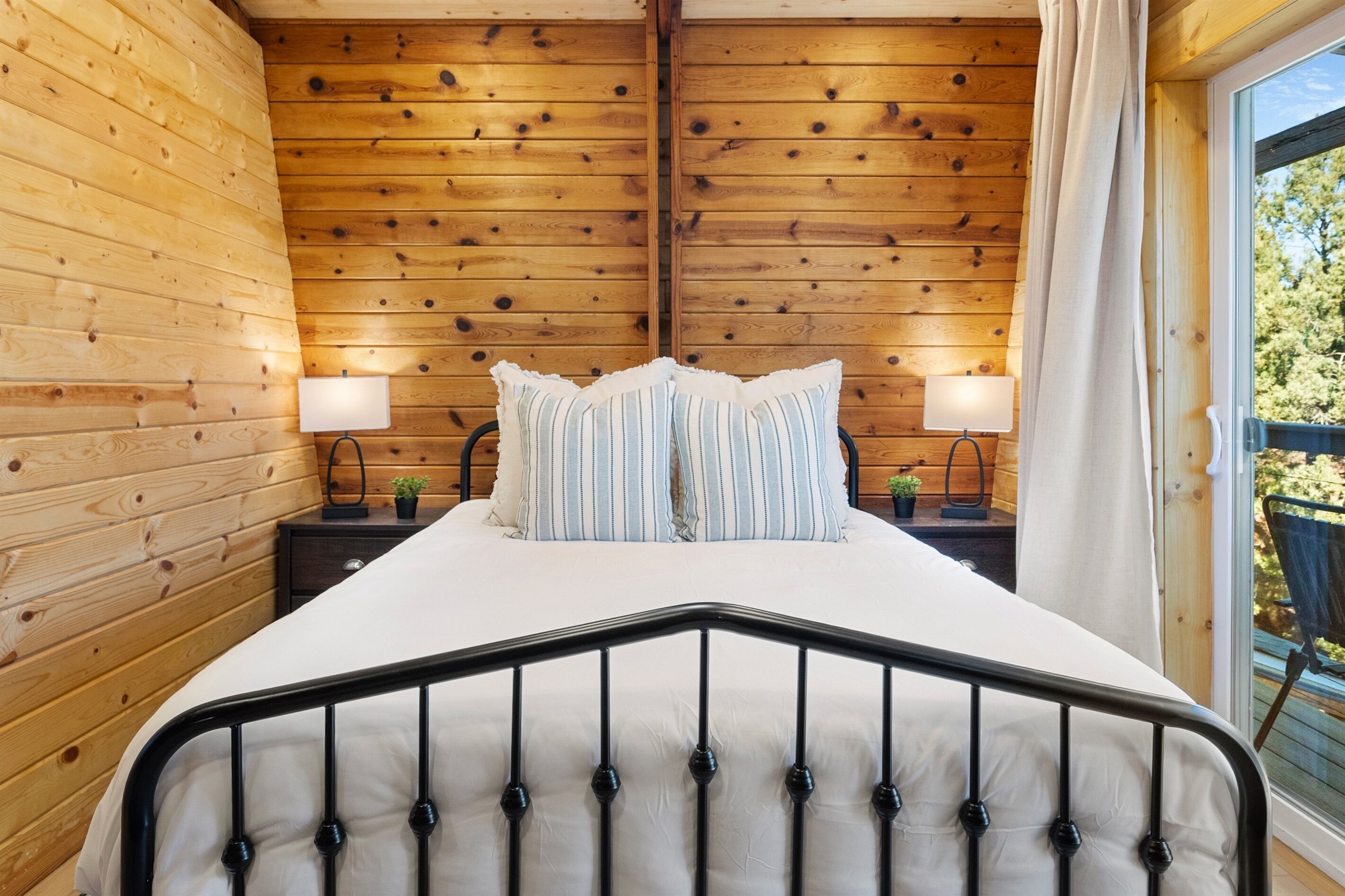Un dormitorio con paneles de madera, una cama, dos mesitas de noche y una ventana con cortinas.