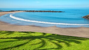 A beach with clear blue water, a sandy shore, and a grassy area with shadows. - Sea View Studio Playa de Las Americas (Playa de Las Americas)