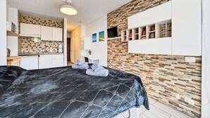 A bedroom with a bed, a kitchenette, a bathroom, and a living area with a TV and shelves. - Sea View Studio Playa de Las Americas (Playa de Las Americas)