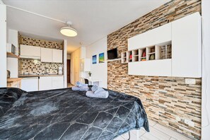 A bedroom with a bed, a kitchenette, a bathroom, and a living area with a TV and shelves. - Sea View Studio Playa de Las Americas (Playa de Las Americas)