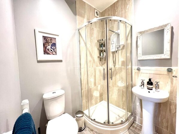 A bathroom with a glass shower enclosure, a toilet, a sink, and a framed picture on the wall.