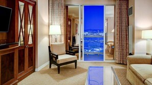 Ein Hotelzimmer mit Fernseher, einem Sessel, einer Couch, einem Glastisch und Meerblick.
