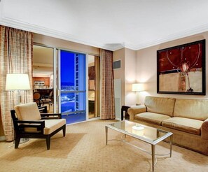 Une chambre d’hôtel avec un canapé, un fauteuil, une table basse en verre et un tableau au mur.