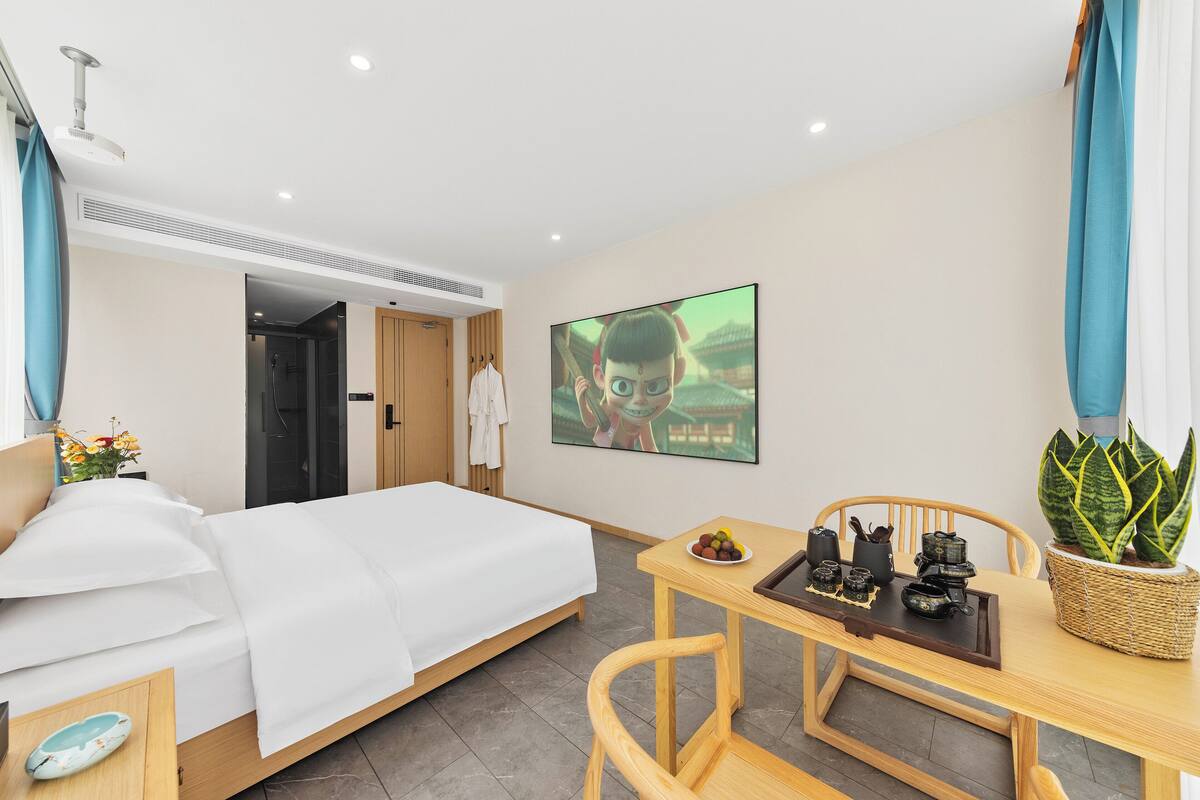 Habitación de hotel con cama, escritorio con planta, televisor montado en la pared y zona de ducha.