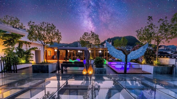 A rooftop terrace with a glass floor, a seating area with a view of the night sky, and a large wing-shaped light fixture. - 12C Baiyujing Hot Spring Resort Furong (Xiangxi)