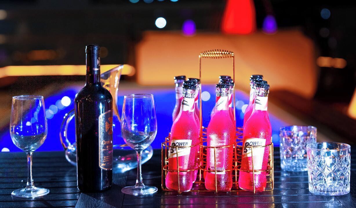 A bottle of wine, several glasses, and a rack of pink bottles on a table.