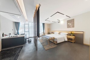 A modern hotel room with a large bed, bedside table, and a built-in desk.