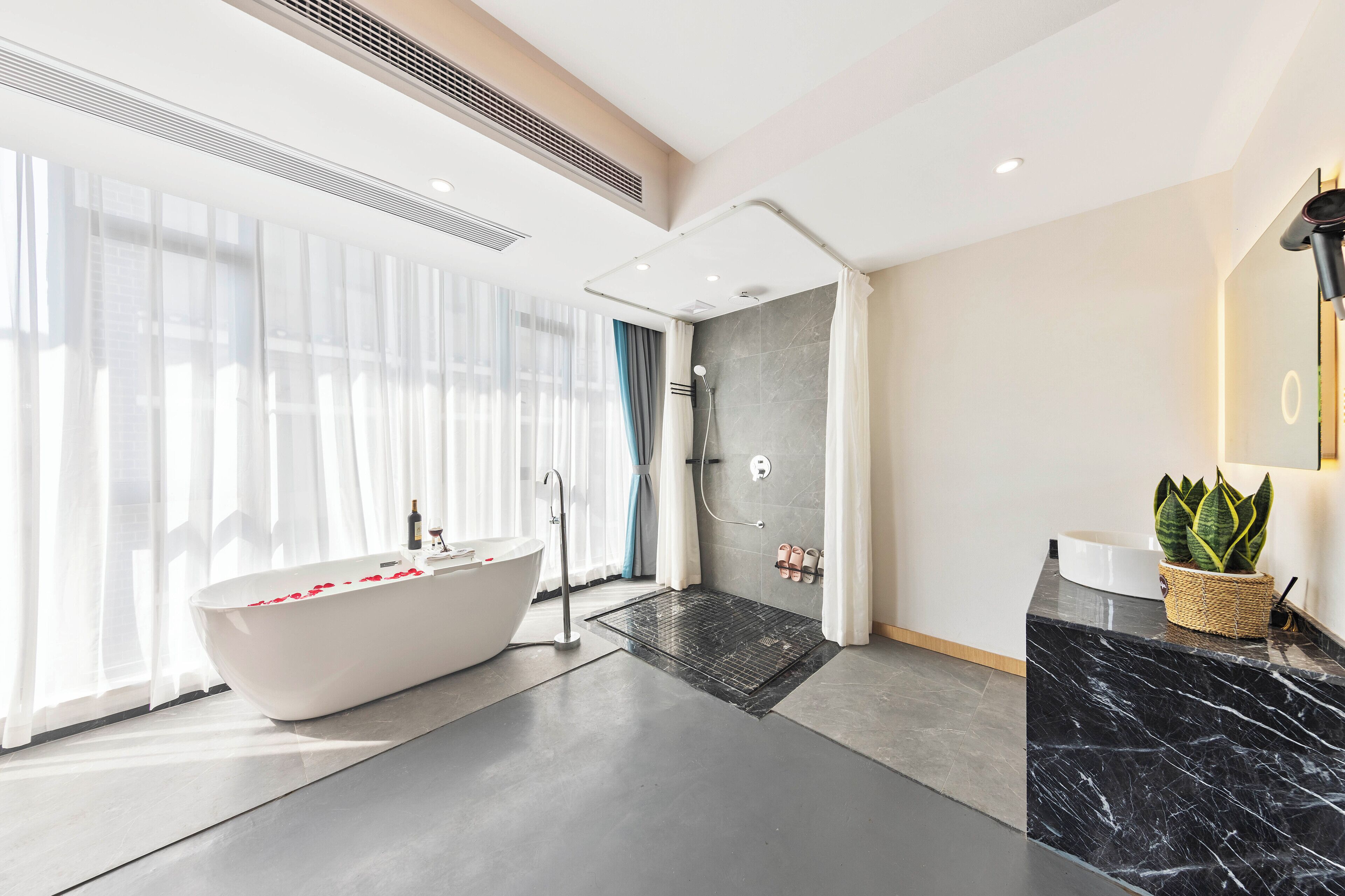 A modern bathroom with a freestanding bathtub, a shower area, and a marble countertop with a potted plant.