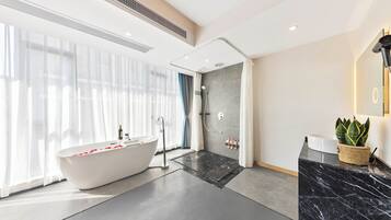 A modern bathroom with a freestanding bathtub, a shower area, and a marble countertop with a potted plant.